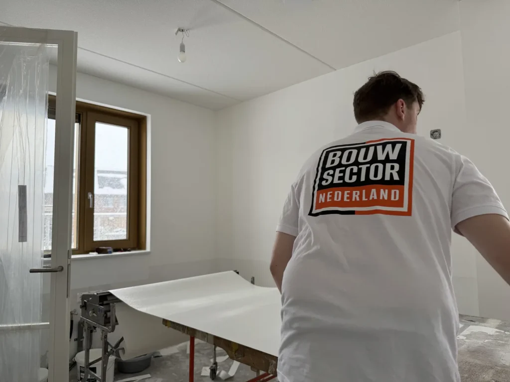 Behanger in een wit shirt met het logo van Bouwsector Nederland rolt een baan renovlies uit op de plaktafel